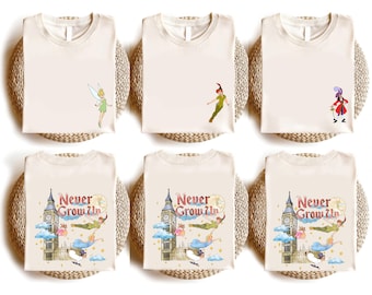 May include: Cream-colored t-shirts featuring Peter Pan characters and imagery. Designs include Tinkerbell, Peter Pan, Captain Hook, and a graphic with the text "Never Grow Up" with Big Ben and flying figures. The shirts are folded on woven mats.