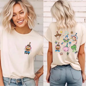 Puede incluir: Camiseta color crema con una imagen de dibujos animados de Mr. Potato Head en la parte delantera, con el nombre "Amp" debajo. La parte posterior de la camiseta muestra varios personajes de Toy Story, incluyendo Woody, Buzz Lightyear y Rex.