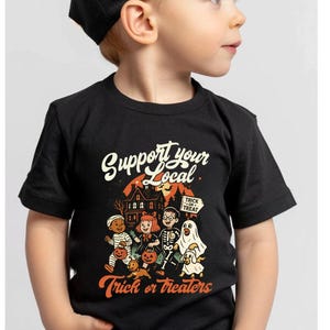 A young boy wearing a black t-shirt with a Halloween-themed graphic and text printed on it.