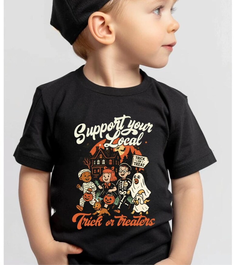 A young boy wearing a black t-shirt with a Halloween-themed graphic and text printed on it.