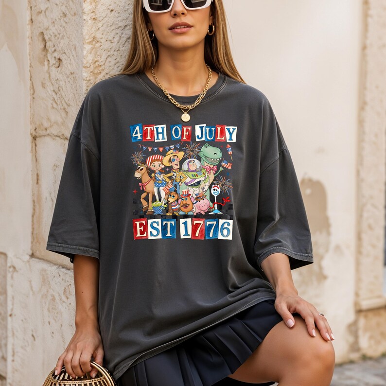 A woman wearing a black t-shirt with a graphic design celebrating the 4th of July, featuring various cartoon characters and fireworks.
