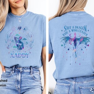 May include: A light blue t-shirt with a graphic design of a person with wings and the text "XADDY" on the front. The back of the shirt has a graphic design of a dragon with the text "Save a Dragon + Ride a Wing Leader".