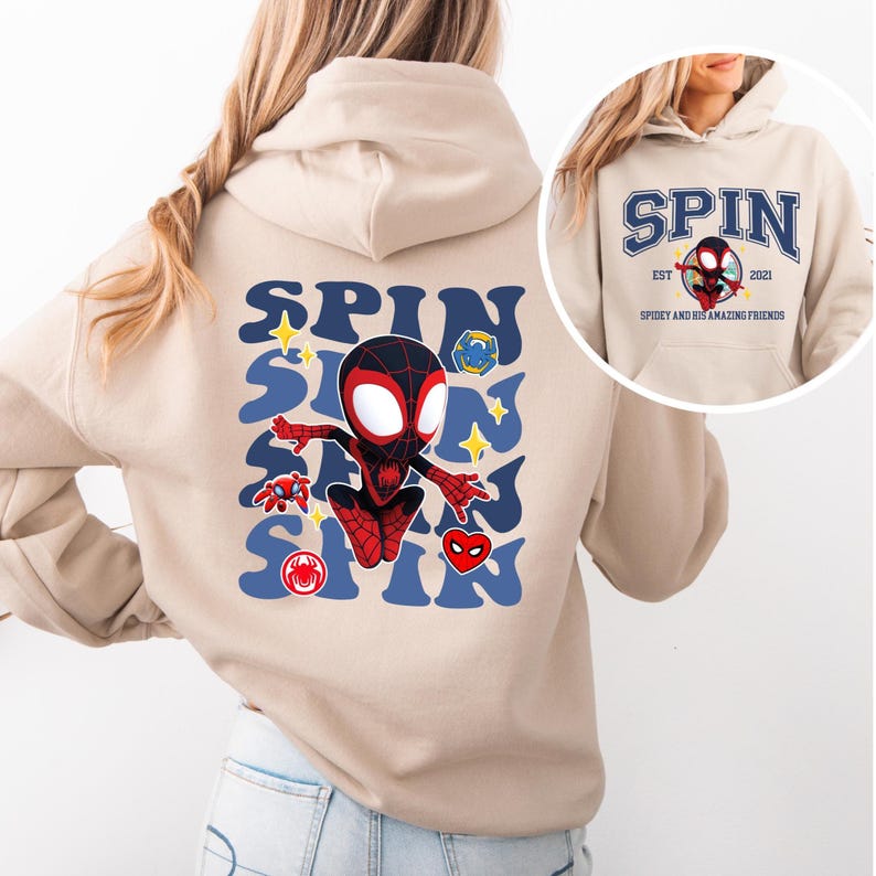A woman wearing a beige hoodie with a graphic of Spider-Man printed on the back.