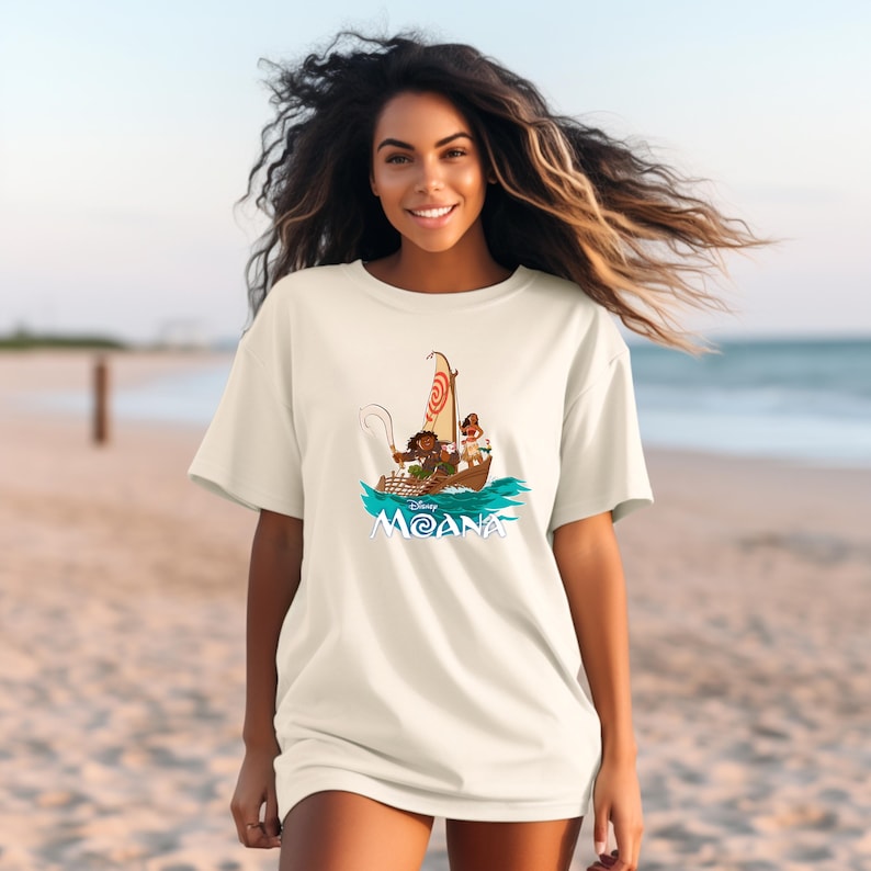 May include: White t-shirt with a graphic of Moana and Maui sailing on a boat. The text "Disney Moana" is printed below the image.