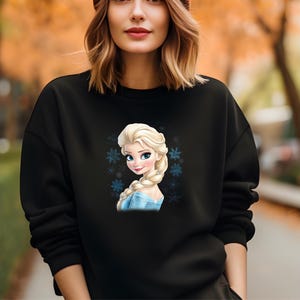 May include: Black sweatshirt with a graphic print of a cartoon character with blonde hair and a blue dress. The character is surrounded by snowflakes.