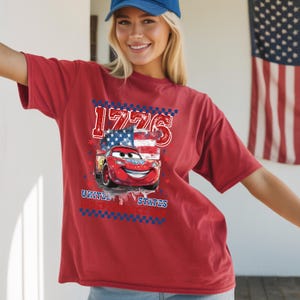 A smiling woman wearing a red t-shirt with a graphic of a red car and an American flag design.