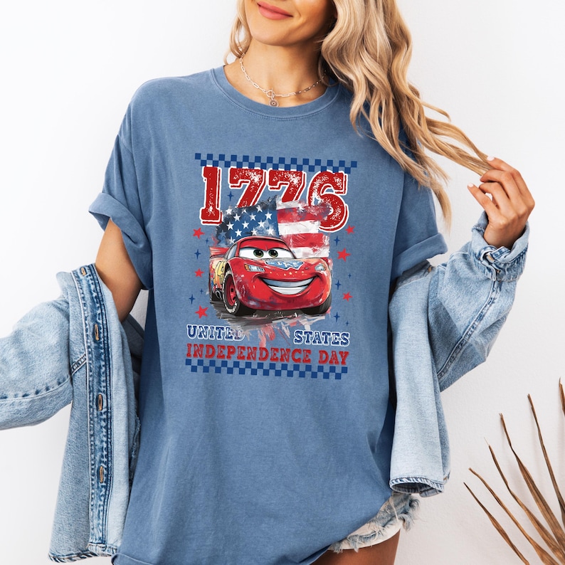 A woman wearing a blue t-shirt with a graphic of a red car and an American flag, along with the text "1776" and "United States Independence Day".