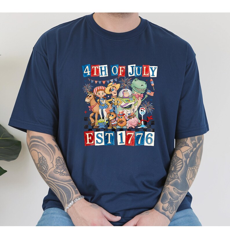 A person wearing a blue t-shirt with a graphic design depicting various cartoon characters and fireworks, celebrating the 4th of July.