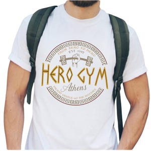 A white t-shirt with a graphic design featuring a fist and the text "HERO GYM Athens" printed on it.