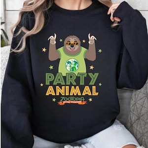 May include: Black sweatshirt featuring a cartoon sloth wearing sunglasses and a green shirt with a world map design. The text "PARTY ANIMAL" is in green and yellow, with "ZOOTOPIA BETTER TOGETHER" below. Yellow stars surround the sloth and text.