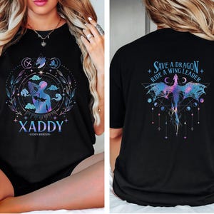 May include: Black t-shirt with a graphic design featuring a person with wings and the text "XADDY - LAUREN ROBINSON" on the front. The back of the shirt features a dragon with the text "Save a Dragon Ride a Wing Leader".