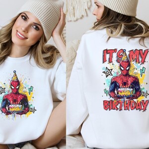 A woman wearing a white sweater with a Spiderman graphic and the text "It's my birthday" printed on the back.