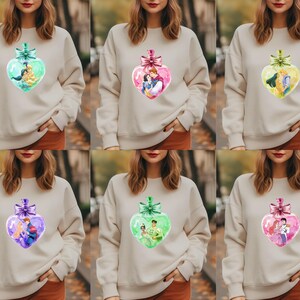 Puede incluir: Seis sudaderas diferentes con un dise&ntilde;o de adorno en forma de coraz&oacute;n que presenta una pareja de una pel&iacute;cula de Disney. Cada sudadera es de un color diferente: verde, rosa, morado, azul, amarillo y naranja.