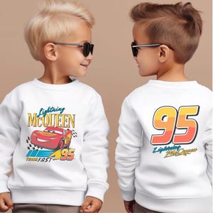 May include: Two white sweatshirts with a Cars theme. One sweatshirt features a red race car with the text "Lightning McQueen" and "Think Fast" on the front. The other sweatshirt has the number "95" with the text "Lightning McQueen" on the back.