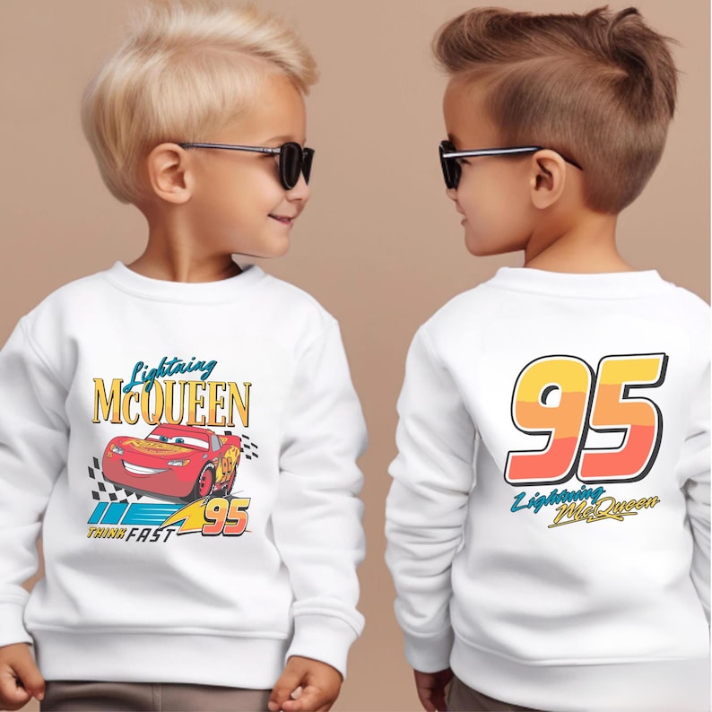 May include: Two white sweatshirts with a Cars theme. One sweatshirt features a red race car with the text "Lightning McQueen" and "Think Fast" on the front. The other sweatshirt has the number "95" with the text "Lightning McQueen" on the back.