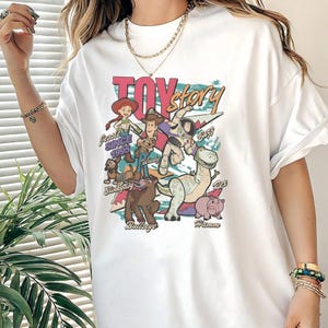 A person wearing a white t-shirt with a colorful graphic of characters from the Toy Story movie.