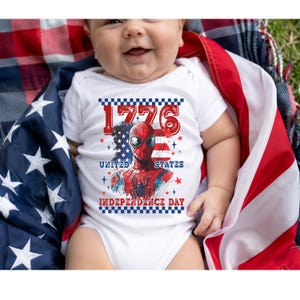 May include: A white baby bodysuit with a graphic of Spider-Man and the text "1776 United States Independence Day". The baby is wrapped in an American flag.