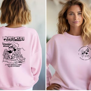 May include: Pink sweatshirt with a black and white graphic of Mickey Mouse on a steamboat. The text "Mickey Mouse Steamboat Willie" is printed above the graphic. The text "A Walt Disney Comic by UB Iwerks" is printed below the graphic.
