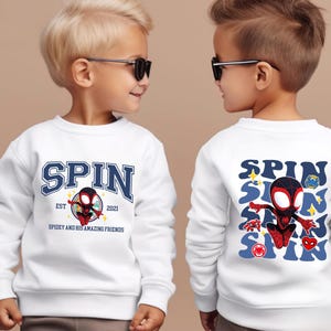 Two young boys wearing white sweatshirts with a Spider-Man design and text printed on them.