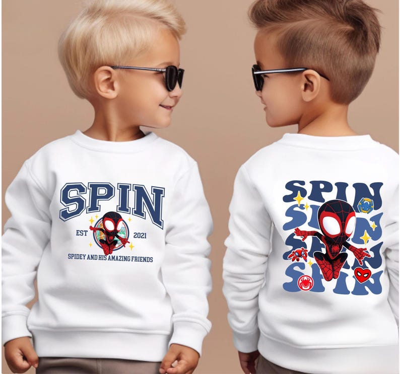 Two young boys wearing white sweatshirts with a Spider-Man design and text printed on them.