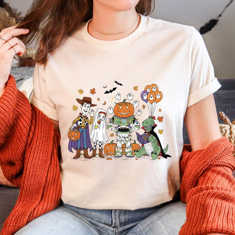 A woman wearing a white t-shirt with a Halloween-themed graphic of characters from Toy Story, including Woody, a pumpkin, and other spooky and festive elements.