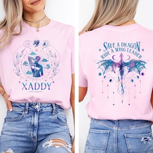 May include: Pink t-shirt with a graphic design of a woman with wings and the text "XADDY" on the front. The back of the shirt has a graphic design of a dragon with the text "Save a Dragon, Ride a Wing Leader".