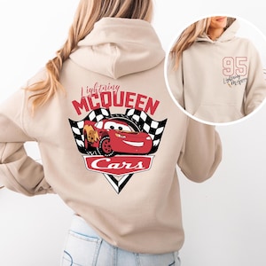May include: Beige hoodie with a red Lightning McQueen Cars graphic on the back. The front of the hoodie has a white number 95 and the text "Lightning McQueen" in black.
