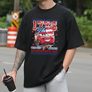 A person wearing a black t-shirt with a graphic design featuring a red car and an American flag, along with the text "1776" and "United States Independence Day".
