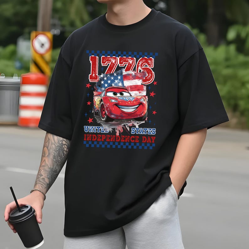 A person wearing a black t-shirt with a graphic design featuring a red car and an American flag, along with the text "1776" and "United States Independence Day".