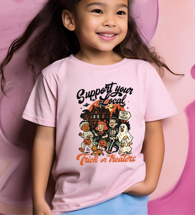 A young girl wearing a pink t-shirt with a Halloween-themed graphic and text, smiling at the camera.