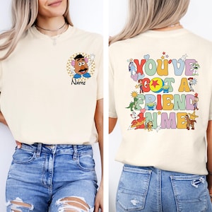 May include: Cream-colored t-shirt featuring a Mr. Potato Head graphic with the word "Name" below it. The back of the shirt displays the phrase "You've Got A Friend In Me" with various cartoon characters.