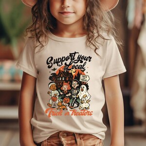 A young girl wearing a white t-shirt with a graphic design featuring Halloween-themed characters and text.