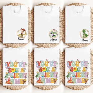 May include: White t-shirts with Toy Story character graphics. The shirts feature Woody, Buzz Lightyear, and Rex, with the word "Name" below each character. Other shirts display the text "You've Got A Friend In Me" in colorful letters.