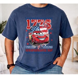 A man wearing a blue t-shirt with a graphic design featuring a red car and an American flag, along with the text "1776" and "United States Independence Day".