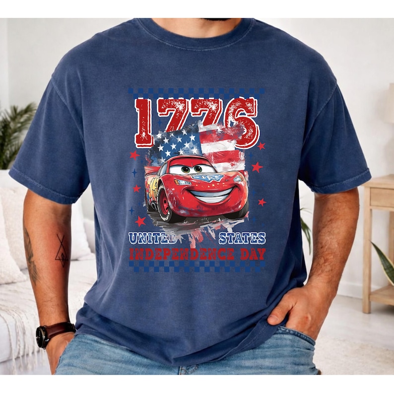 A man wearing a blue t-shirt with a graphic design featuring a red car and an American flag, along with the text "1776" and "United States Independence Day".