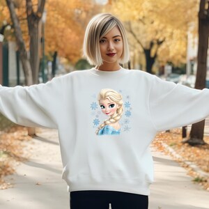 May include: White sweatshirt with a printed image of a cartoon character with blonde hair and blue eyes. The character is wearing a blue dress and has snowflakes around her.