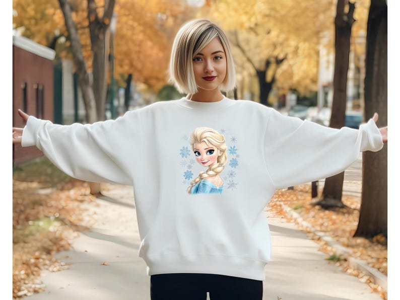 May include: White sweatshirt with a printed image of a cartoon character with blonde hair and blue eyes. The character is wearing a blue dress and has snowflakes around her.
