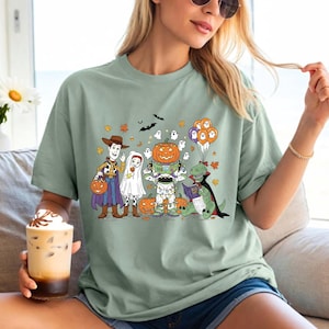 A woman wearing a green t-shirt with a Halloween-themed graphic of characters from Toy Story, including Woody, a pumpkin, and other spooky and festive elements.