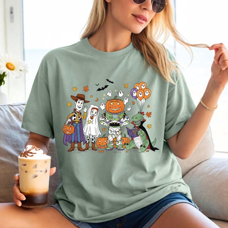 A woman wearing a green t-shirt with a Halloween-themed graphic of characters from Toy Story, including Woody, a pumpkin, and other spooky and festive elements.