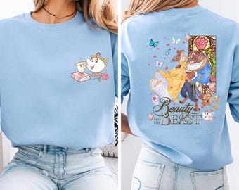 May include: Light blue sweatshirt featuring a cartoon design from Beauty and the Beast. The front has a teacup, teapot, and book. The back has Belle and the Beast with the words "Beauty and the Beast".