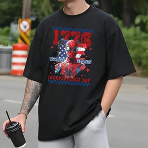 May include: Black t-shirt featuring a graphic of Spider-Man with an American flag design. The text "1776", "United States", and "Independence Day" are also displayed. The shirt has short sleeves and a relaxed fit.
