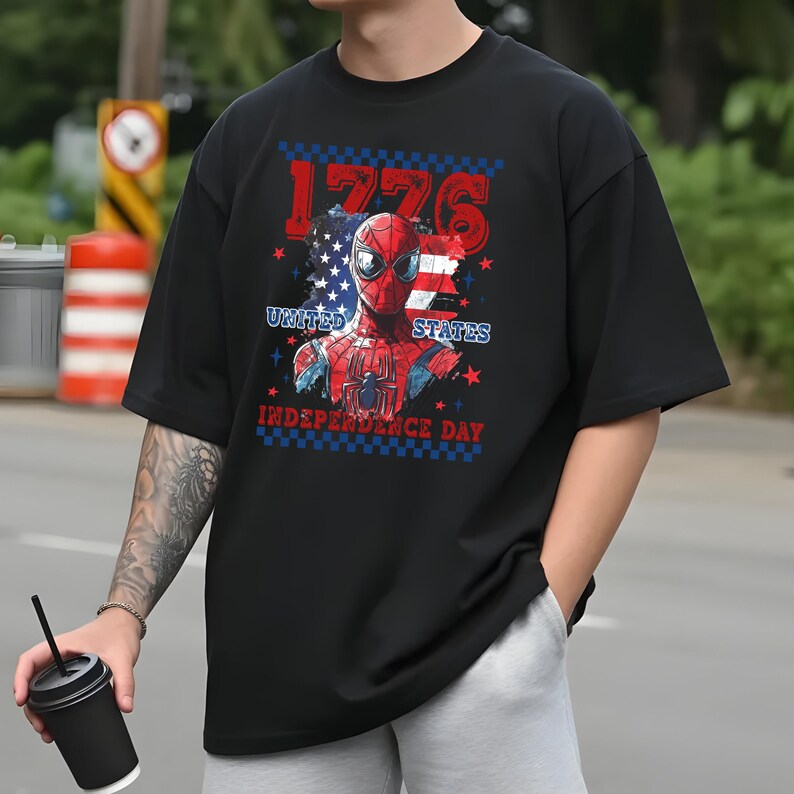 May include: Black t-shirt featuring a graphic of Spider-Man with an American flag design. The text "1776", "United States", and "Independence Day" are also displayed. The shirt has short sleeves and a relaxed fit.