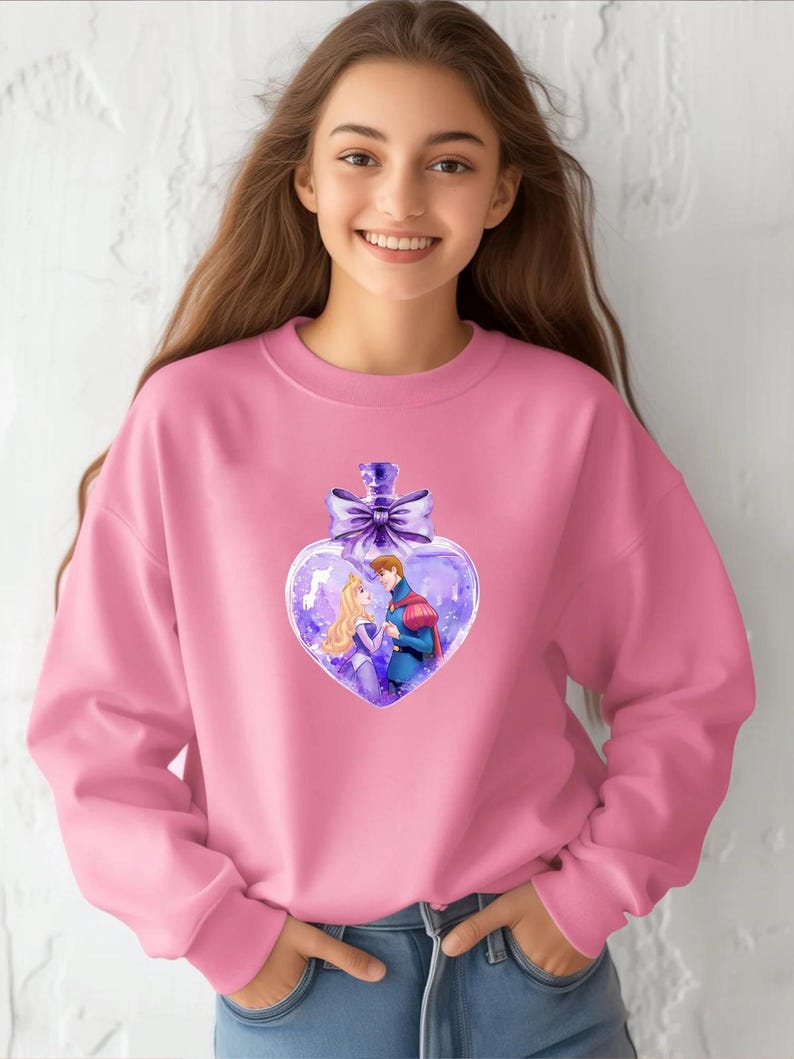 Puede incluir: Sudadera rosa con un dise&ntilde;o de botella en forma de coraz&oacute;n morado que presenta un pr&iacute;ncipe y una princesa en su interior. La botella tiene un lazo morado en la parte superior.