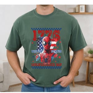 May include: Green t-shirt featuring a graphic of Spider-Man with the American flag and the text "1776 United States Independence Day". The design is in red, white, and blue.