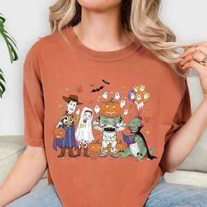 A woman wearing a t-shirt with a Halloween-themed graphic of characters from Toy Story, including Woody, a pumpkin, and other spooky and festive elements.