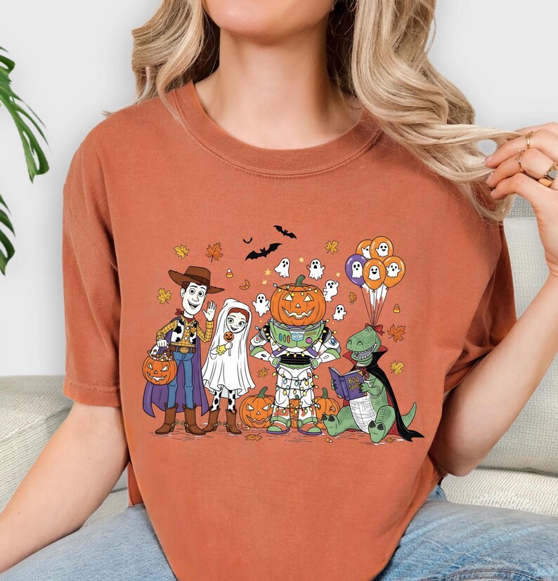 A woman wearing a t-shirt with a Halloween-themed graphic of characters from Toy Story, including Woody, a pumpkin, and other spooky and festive elements.