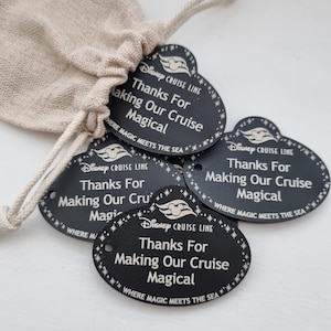 May include: Black oval tags with the text "Disney Cruise Line Thanks For Making Our Cruise Magical" and a Mickey Mouse icon. The tags are in a beige drawstring bag. The text "Where Magic Meets The Sea" is also on the tags.