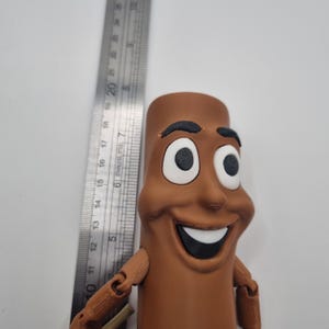 Puede incluir: Una figura de juguete articulada de un personaje de dibujos animados sonriente con ojos grandes y una amplia sonrisa. La figura es de color marr&oacute;n y negro y tiene forma de un palo largo y delgado.