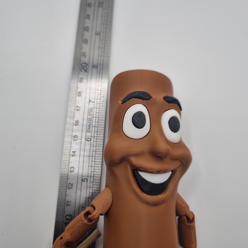 Puede incluir: Una figura de juguete articulada de un personaje de dibujos animados sonriente con ojos grandes y una amplia sonrisa. La figura es de color marr&oacute;n y negro y tiene forma de un palo largo y delgado.