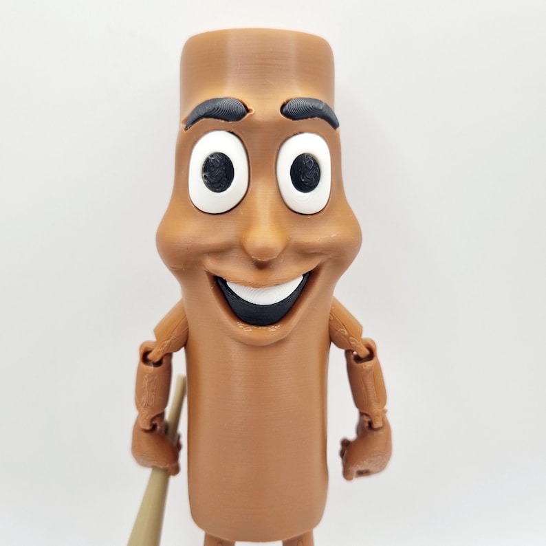 Puede incluir: Una figura de juguete articulada de color marr&oacute;n con una cara sonriente, ojos grandes blancos y una boca negra. La figura tiene forma de un cilindro largo y delgado.